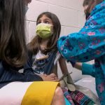 n this Wednesday, March 24, 2021 image from video provided by Duke Health, Alejandra Gerardo, 9, looks up to her mom, Dr. Susanna Naggie, as she gets the first of two Pfizer COVID-19 vaccinations during a clinical trial for children at Duke Health in Durham, N.C. In the U.S. and abroad, researchers are beginning to test younger and younger kids, to make sure the shots are safe and work for each age. (Shawn Rocco/Duke Health via AP)