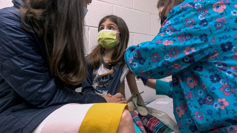 n this Wednesday, March 24, 2021 image from video provided by Duke Health, Alejandra Gerardo, 9, looks up to her mom, Dr. Susanna Naggie, as she gets the first of two Pfizer COVID-19 vaccinations during a clinical trial for children at Duke Health in Durham, N.C. In the U.S. and abroad, researchers are beginning to test younger and younger kids, to make sure the shots are safe and work for each age. (Shawn Rocco/Duke Health via AP)